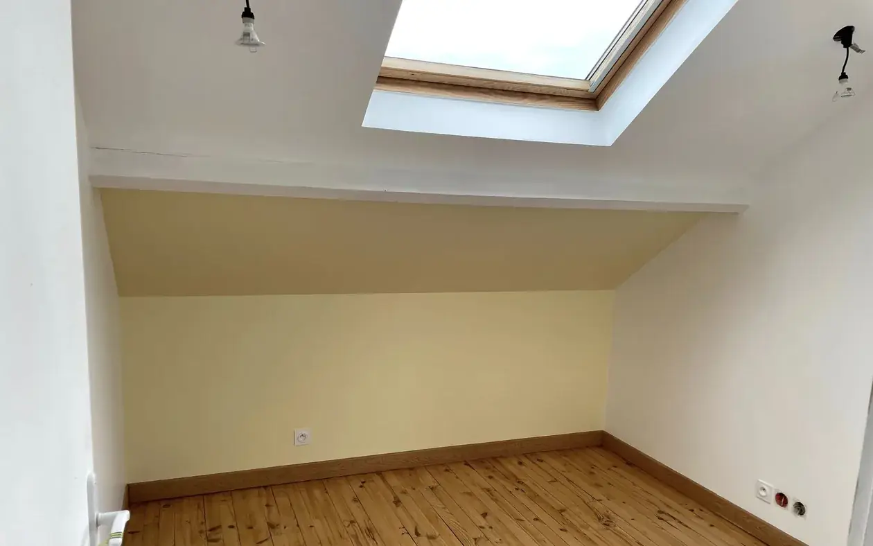 Chambre sous rampant terminée : mur peint en jaune pâle, plafond blanc, fenêtre de toit et parquet en pin d'origine conservé