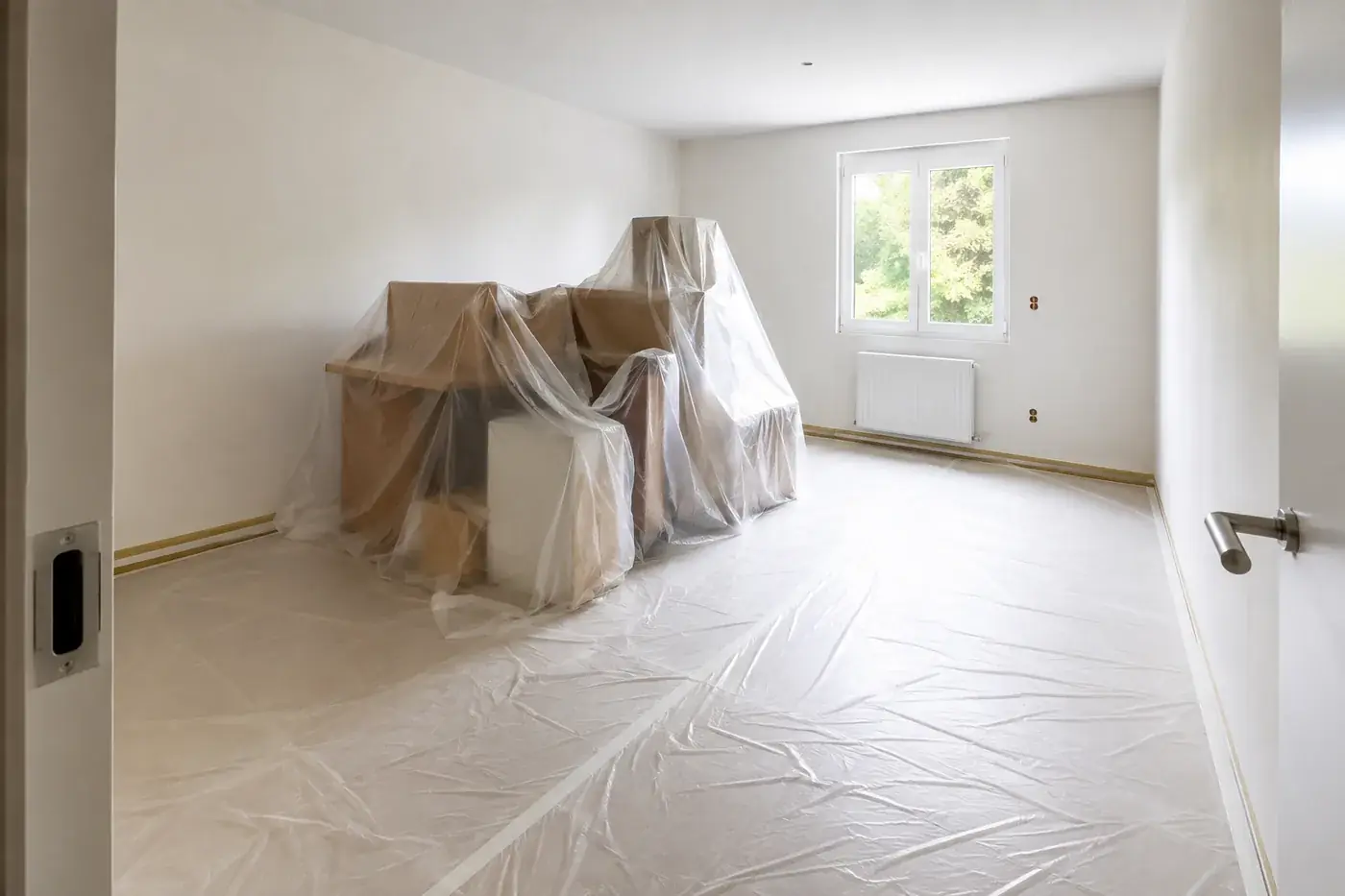 Pièce en cours de chantier : meubles regroupés au centre et protégés par un film plastique, sol entièrement bâché, adhésif de masquage sur les plinthes